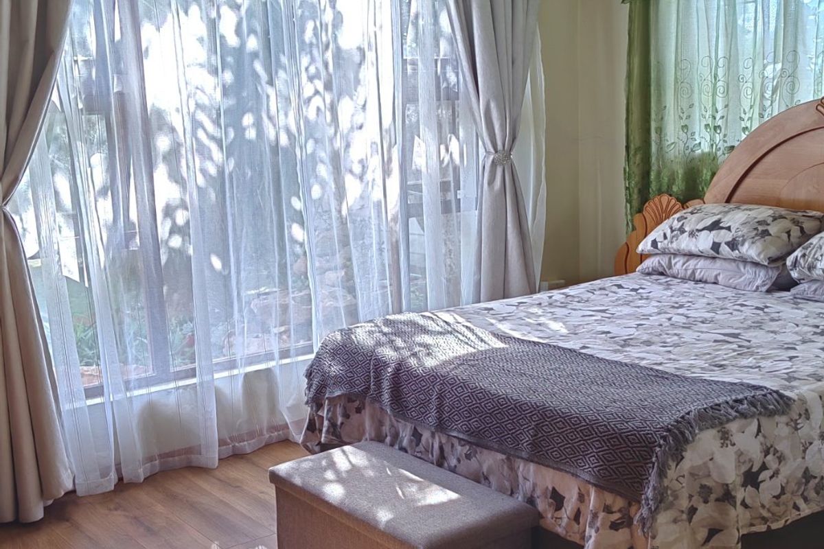 A sunlit bedroom featuring laminate flooring and large windows with layered curtains, offering a bright and comfortable living space.
