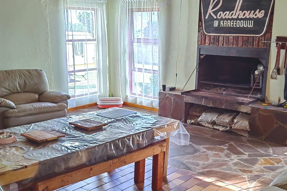 Rustic living area featuring a large brick fireplace with stone hearth, exposed timber beam ceiling, and tiled flooring.