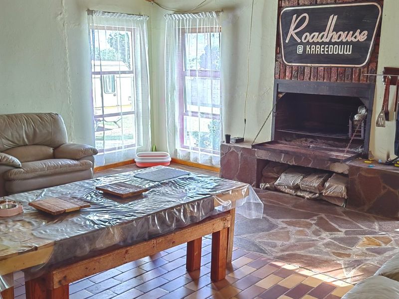 Rustic living area featuring a large brick fireplace with stone hearth, exposed timber beam ceiling, and tiled flooring.