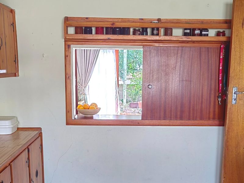 A dated kitchen area featuring wooden cabinetry, a functional serving hatch with integrated shelving, and patterned vinyl flooring.