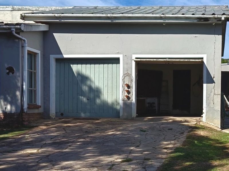 A detached double garage with a metal roof and paved driveway, showing signs of wear on the exterior walls and paving.