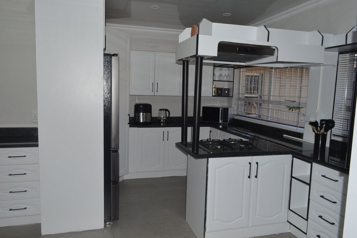 A functional kitchen featuring white cabinetry, contrasting black granite countertops, a built-in gas hob with extractor fan, and modern glossy ceiling finishes.