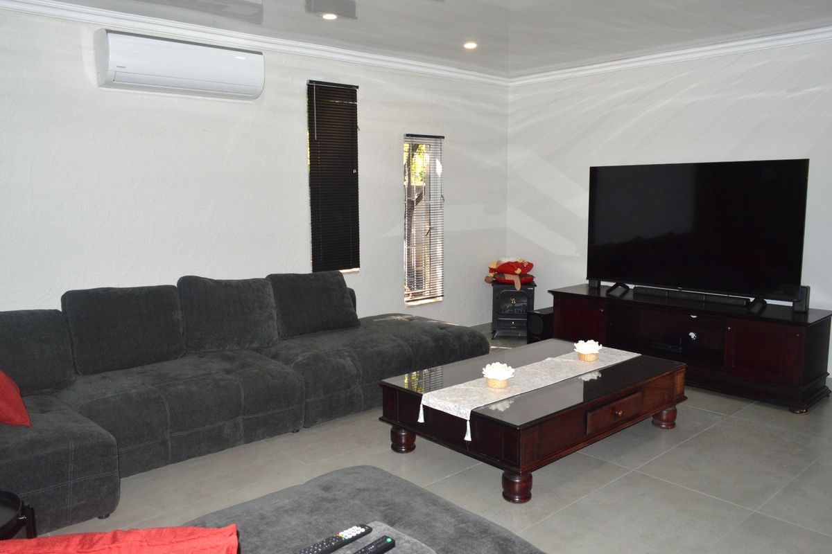 A well-maintained living room featuring tiled flooring, recessed downlighting, and a wall-mounted split-system air conditioner.