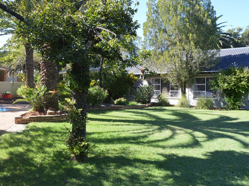 A spacious rear garden featuring a well-maintained lawn, mature trees, and a swimming pool area adjacent to the main house structure.