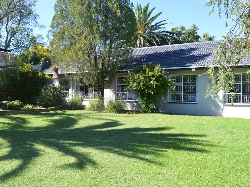 A view of the rear elevation of the house featuring a tiled roof, security bars on windows, and a well-maintained garden area.