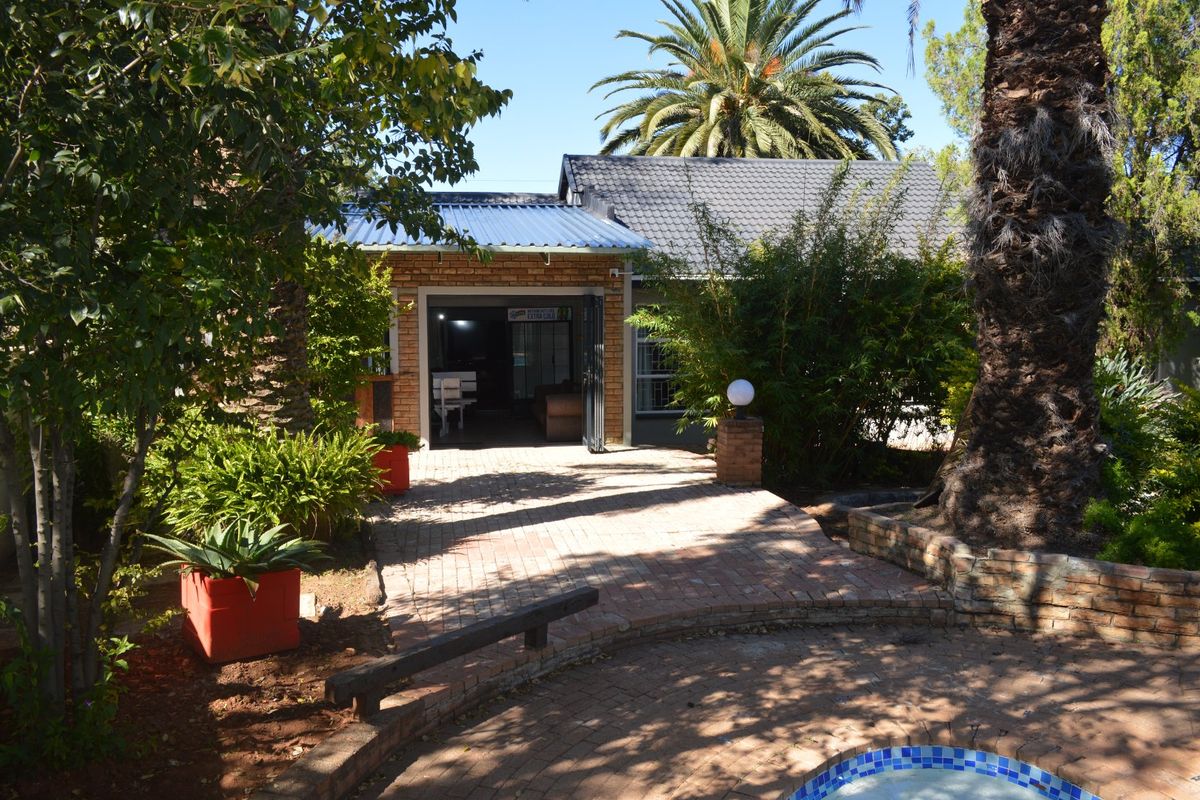 Rear view of the property featuring a brick-paved patio area, swimming pool, and established garden surroundings.