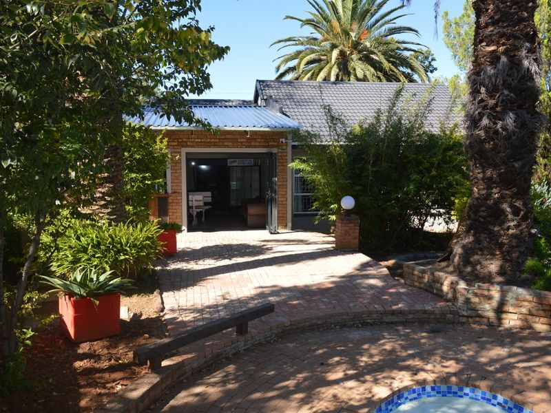 Rear view of the property featuring a brick-paved patio area, swimming pool, and established garden surroundings.
