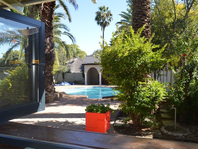 Outdoor pool area featuring a paved patio, swimming pool, and a covered gazebo, surrounded by established trees and garden landscaping.