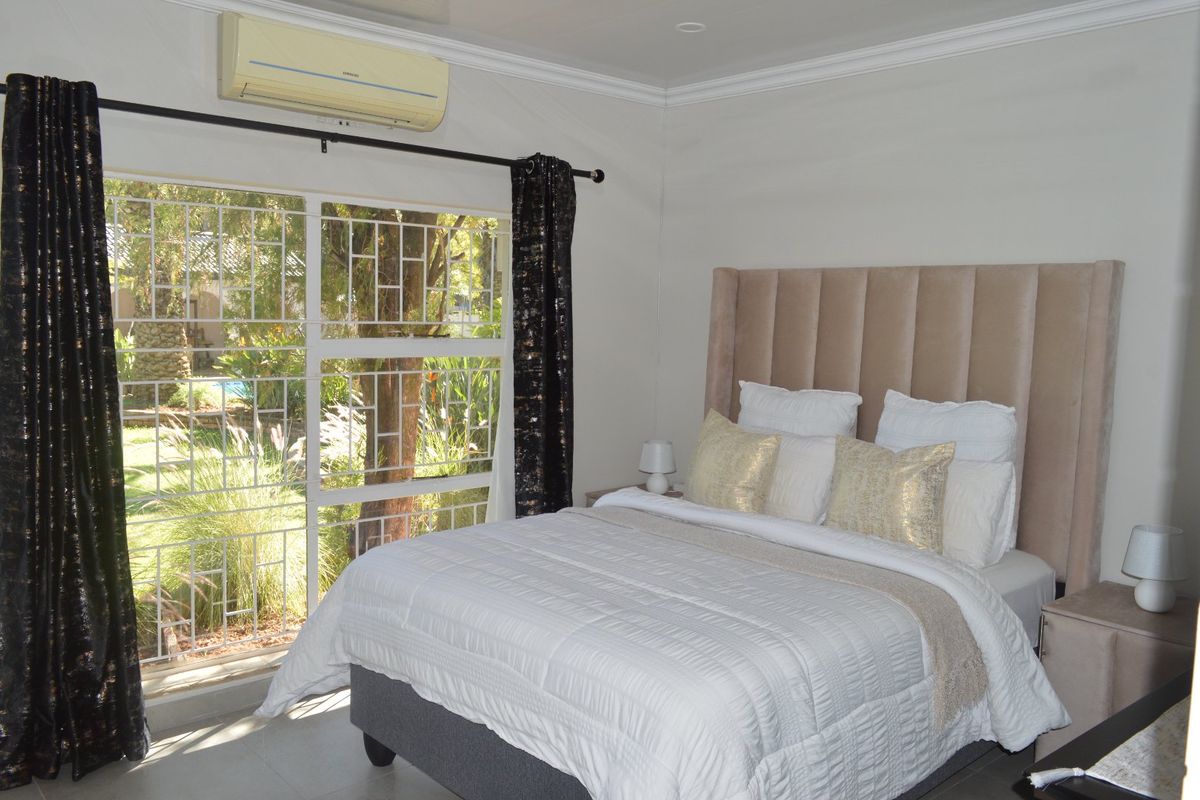 A well-maintained bedroom featuring crown molding, a split-system air conditioner, and a large sliding glass door with security gate overlooking the garden.