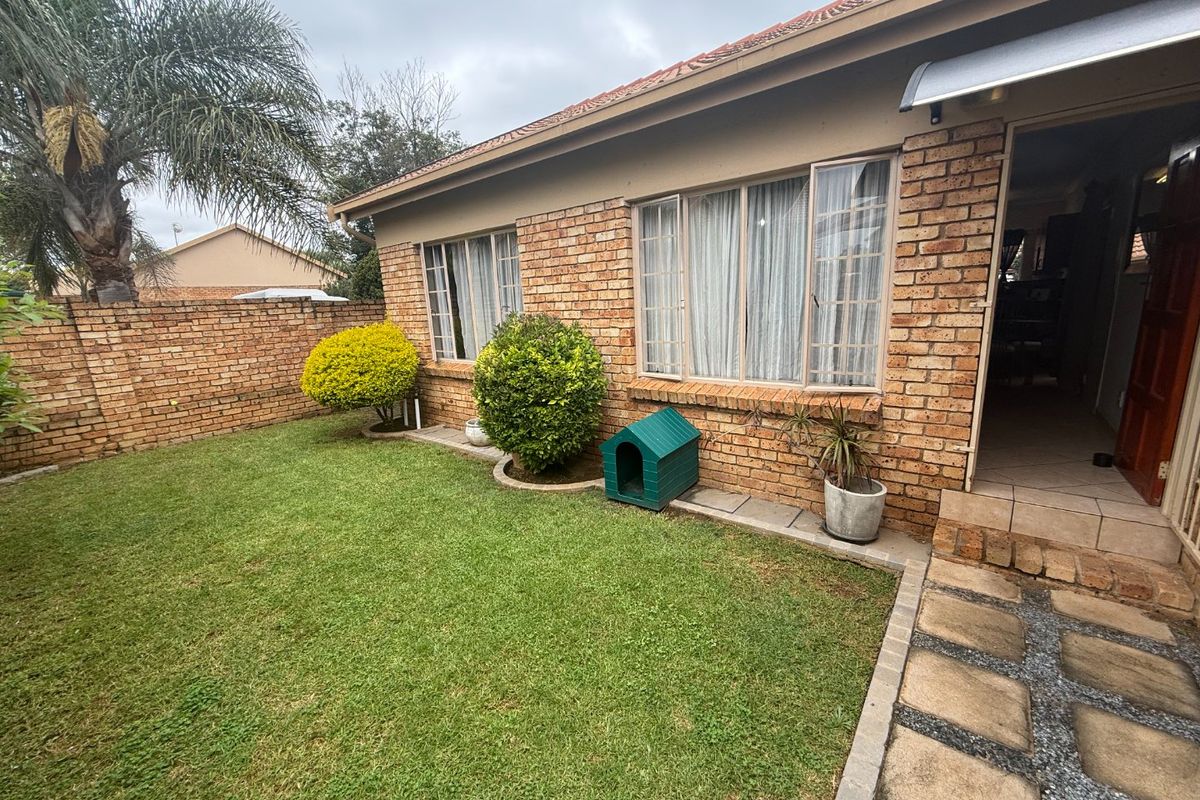 A private rear garden featuring a well-maintained lawn, face brick exterior, and a paved walkway leading to the entrance.