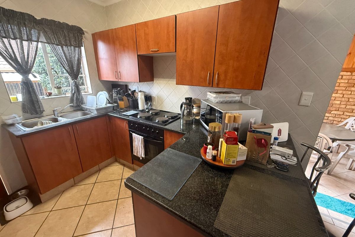 A functional kitchen featuring warm-toned laminate cabinetry, granite countertops, a built-in oven with electric hob, and a double basin sink with tiled backsplash.