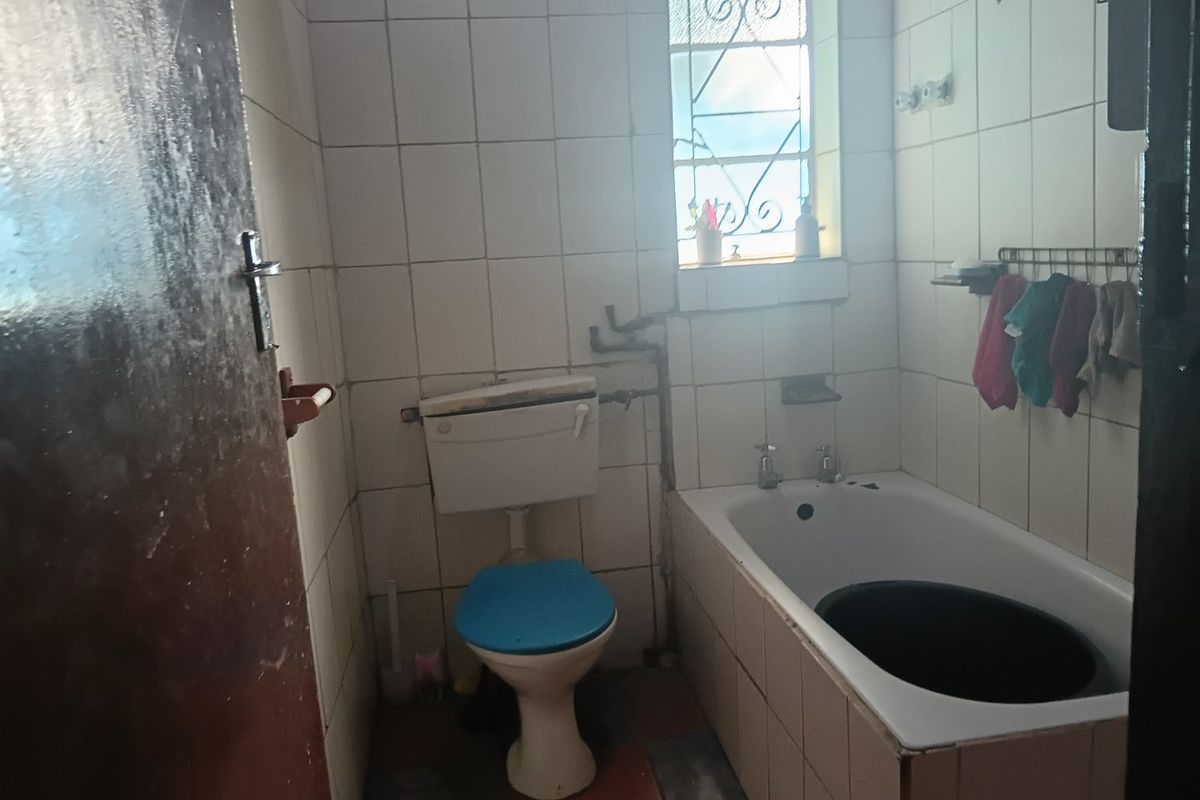 A dated bathroom featuring a standard bathtub, toilet, and tiled finishes. The space requires renovation to update the fixtures and improve overall condition.