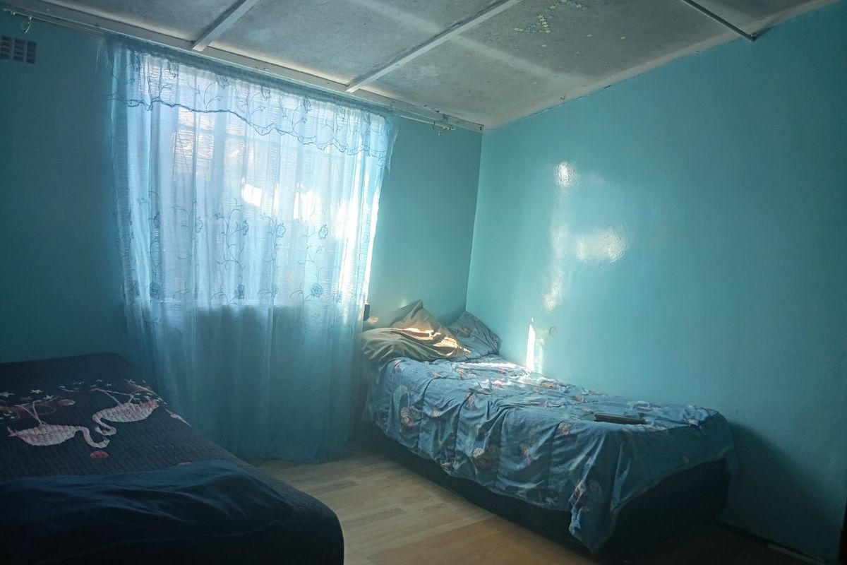 A bedroom featuring laminate flooring and an exposed ceiling grid, requiring cosmetic updates to improve the overall finish and aesthetic appeal.