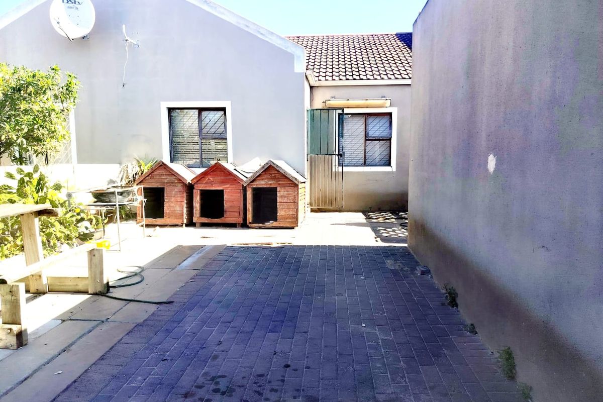 A paved rear courtyard area featuring exterior walls with security-barred windows and a tiled roof section.
