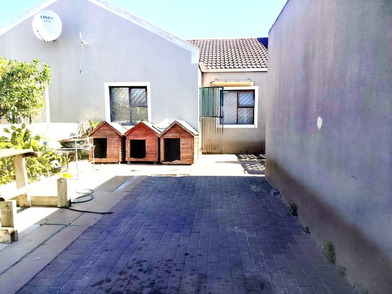 A paved rear courtyard area featuring exterior walls with security-barred windows and a tiled roof section.