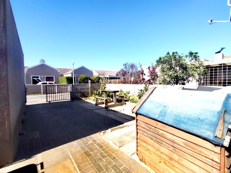A rear exterior area featuring paved surfaces, a boundary wall, and a metal gate, providing access to the property's outdoor space.