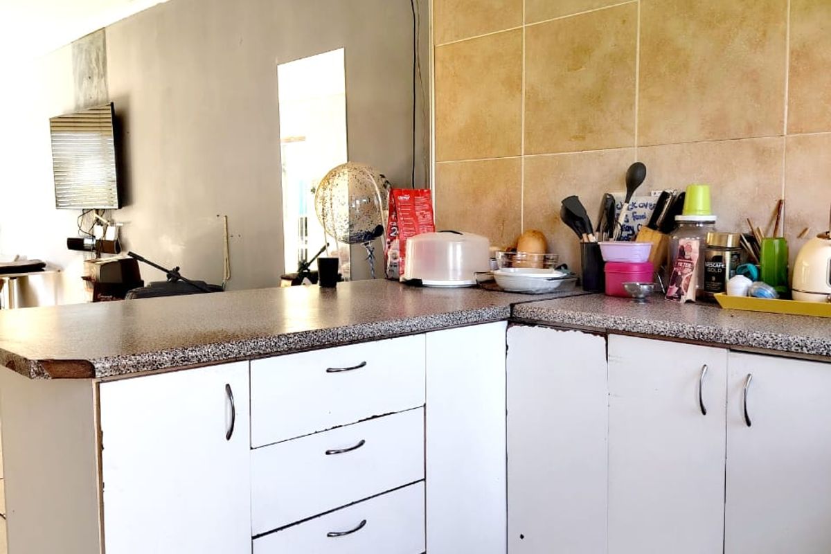 A kitchen area featuring laminate countertops, tiled backsplash, and white cabinetry showing signs of wear, with tiled flooring and pendant lighting.