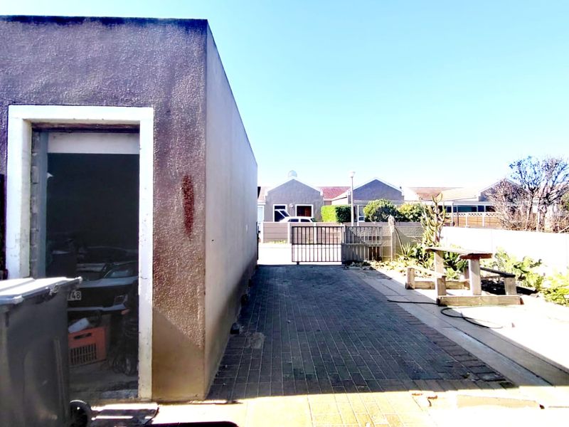 Rear exterior view showing a paved driveway, metal security gate, and a detached garage structure with visible wall weathering.