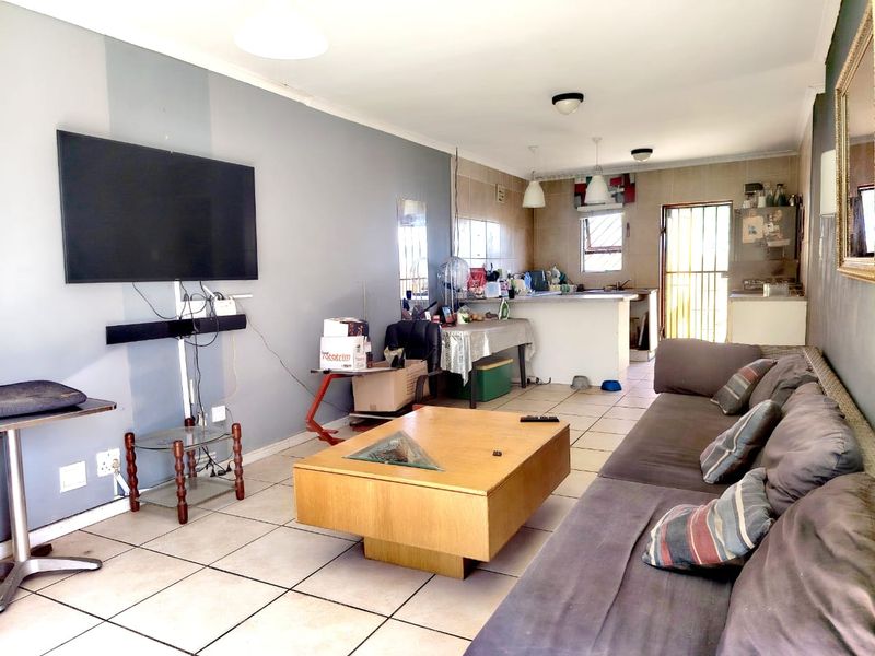 Open-plan living and kitchen area featuring tiled flooring, a breakfast bar, and direct access to an exterior door with a security gate.