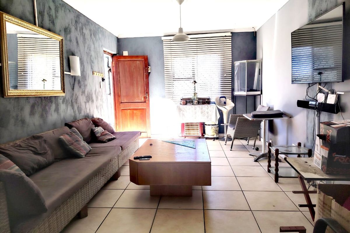 A living room featuring tiled flooring, venetian blinds, and a timber entrance door, requiring cosmetic updates to improve the overall aesthetic.