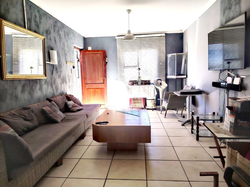A living room featuring tiled flooring, venetian blinds, and a timber entrance door, requiring cosmetic updates to improve the overall aesthetic.