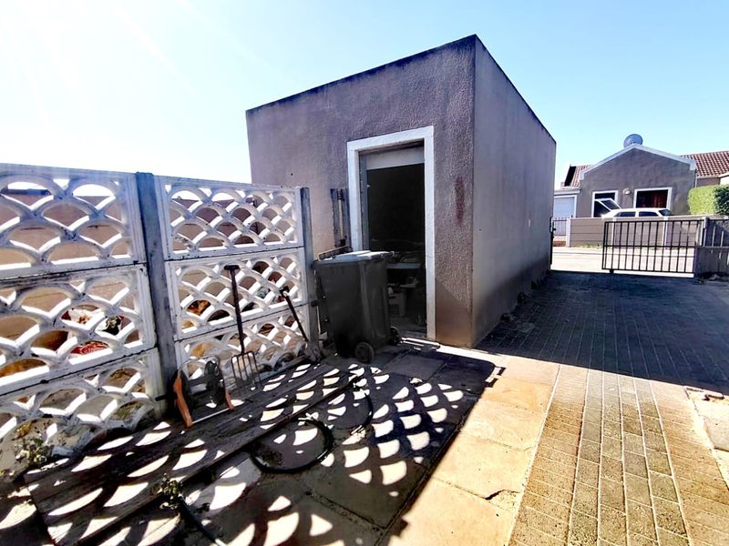 A detached utility structure or storage shed located on a paved driveway, featuring a decorative screen wall and metal gate access.