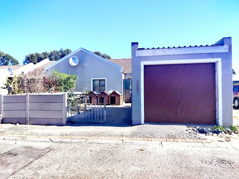 Front exterior view of the property featuring a single garage, paved driveway, and boundary wall with a metal gate.