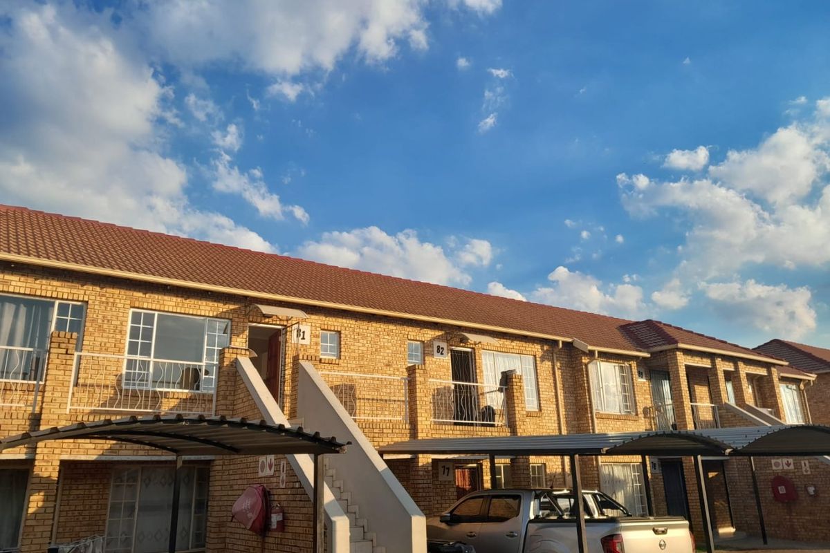 Exterior view of a multi-unit apartment complex featuring face brick construction, tiled roofing, and dedicated metal carport parking bays.