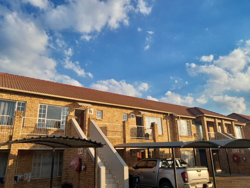 Exterior view of a multi-unit apartment complex featuring face brick construction, tiled roofing, and dedicated metal carport parking bays.
