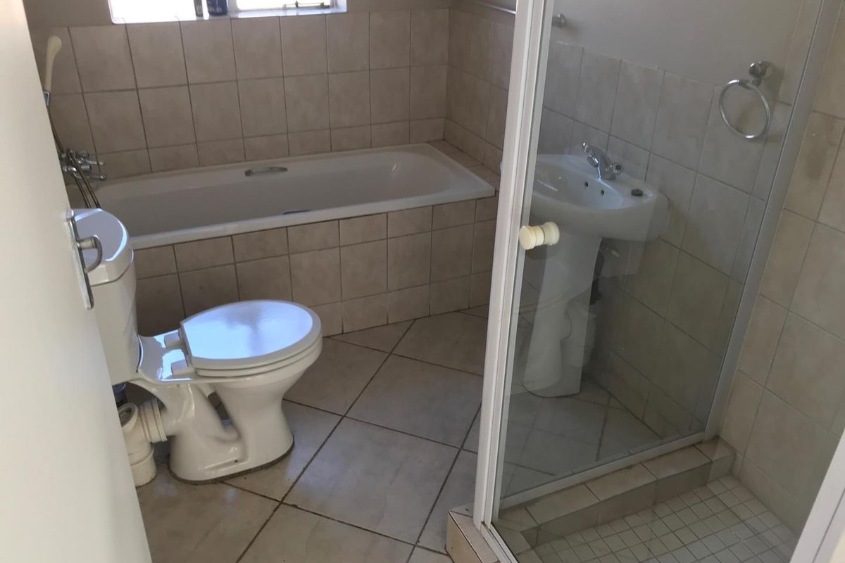 A functional bathroom featuring a built-in bathtub, separate shower enclosure, pedestal basin, and toilet with neutral wall and floor tiling.