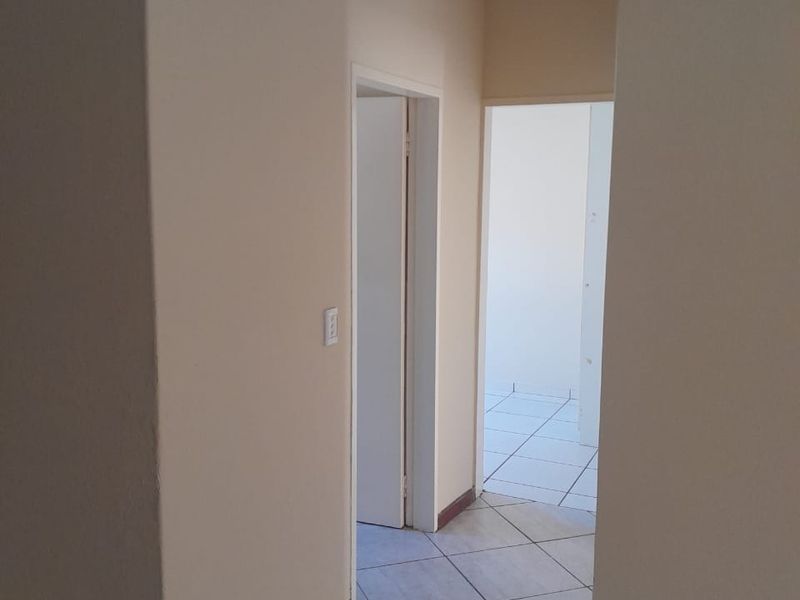 A neutral-toned hallway featuring tiled flooring and access to adjacent rooms, providing a clean and functional transition space within the apartment.