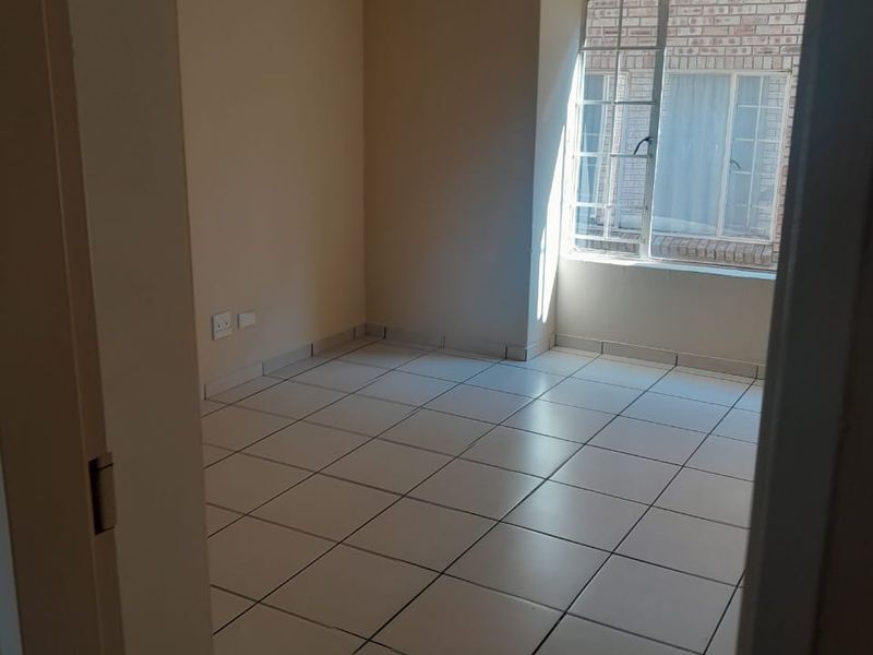 An empty bedroom featuring neutral wall paint, tiled flooring, and a window with security bars, providing a clean and versatile space.