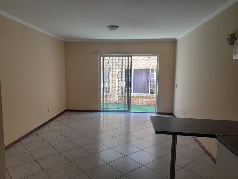 An empty open-plan living area featuring tiled flooring, a breakfast bar, and a sliding glass door leading to an outdoor space.