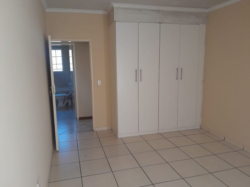 An empty bedroom featuring tiled flooring and built-in cupboards, with an adjacent bathroom visible through the doorway.