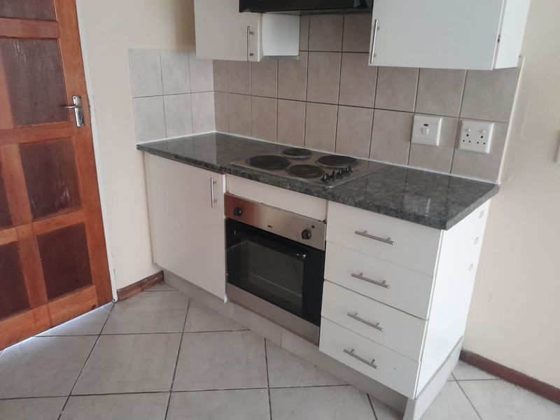 A compact kitchen featuring built-in cabinetry, a stainless steel oven, electric hob, extractor fan, and tiled backsplash with neutral ceramic flooring.