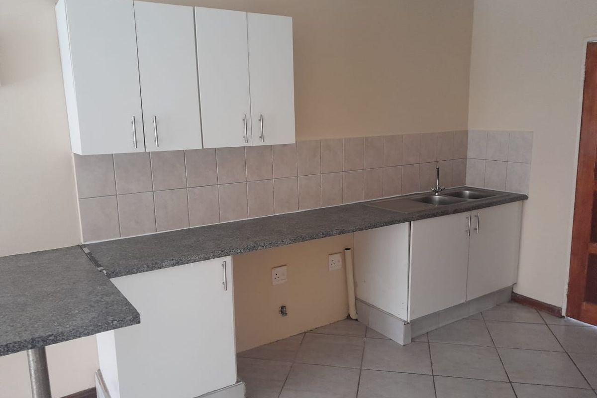 A functional kitchen area featuring white cabinetry, grey laminate countertops, a stainless steel double sink, and neutral tiled flooring.