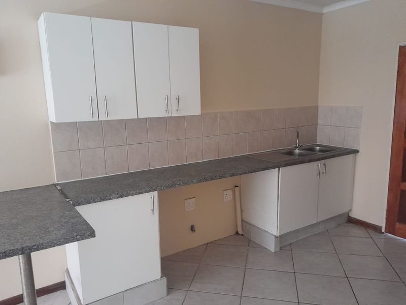 A functional kitchen area featuring white cabinetry, grey laminate countertops, a stainless steel double sink, and neutral tiled flooring.
