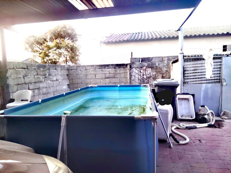 Outdoor paved patio area featuring a metal roof structure and a boundary wall, currently utilized for a portable pool setup.
