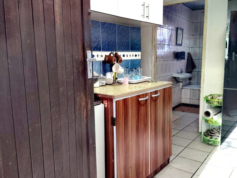 A functional scullery area featuring built-in cabinetry, tiled splashbacks, and tiled flooring, providing additional storage and prep space adjacent to the bathroom.