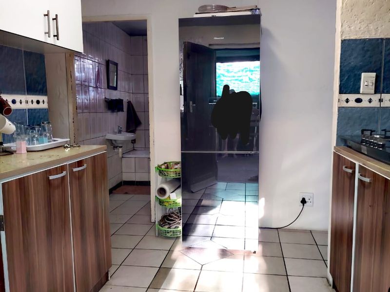 A functional kitchen featuring built-in cabinetry, tiled flooring, and a gas hob, with an adjacent bathroom area visible through the doorway.