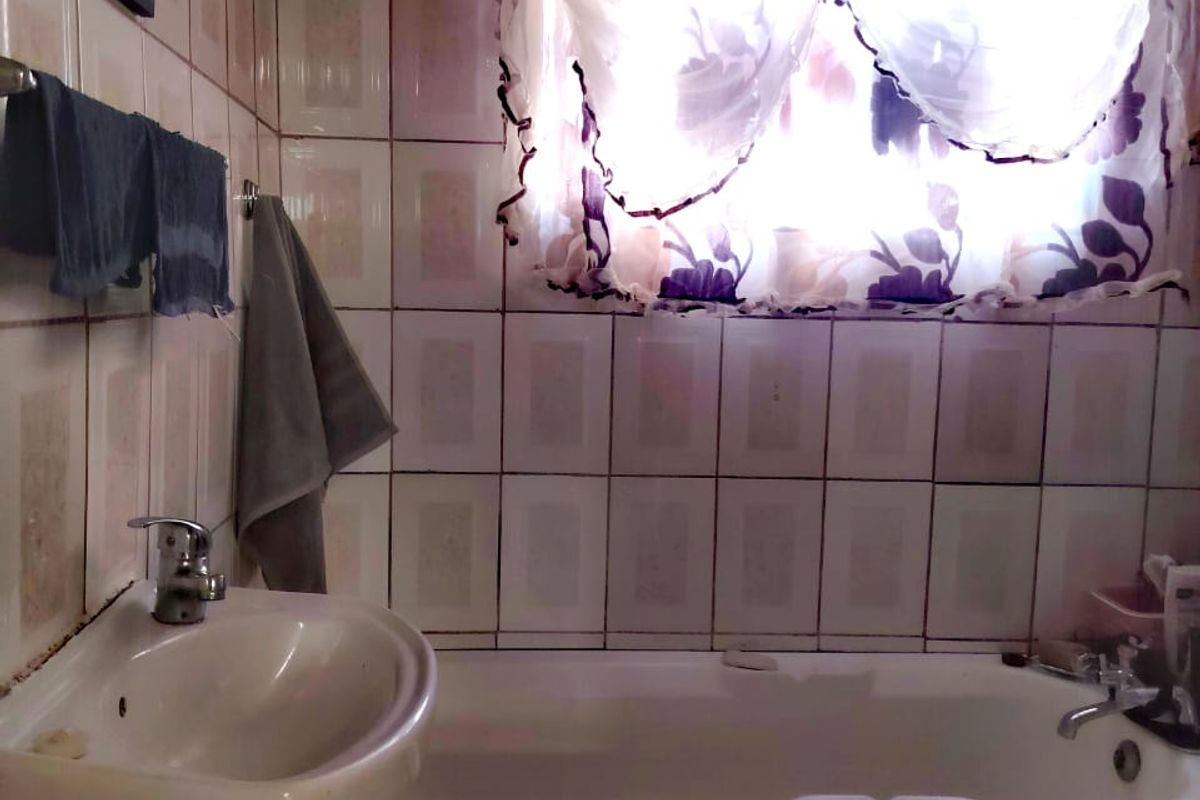 A dated bathroom featuring a wall-mounted basin and a built-in bathtub with full-height ceramic wall tiling.