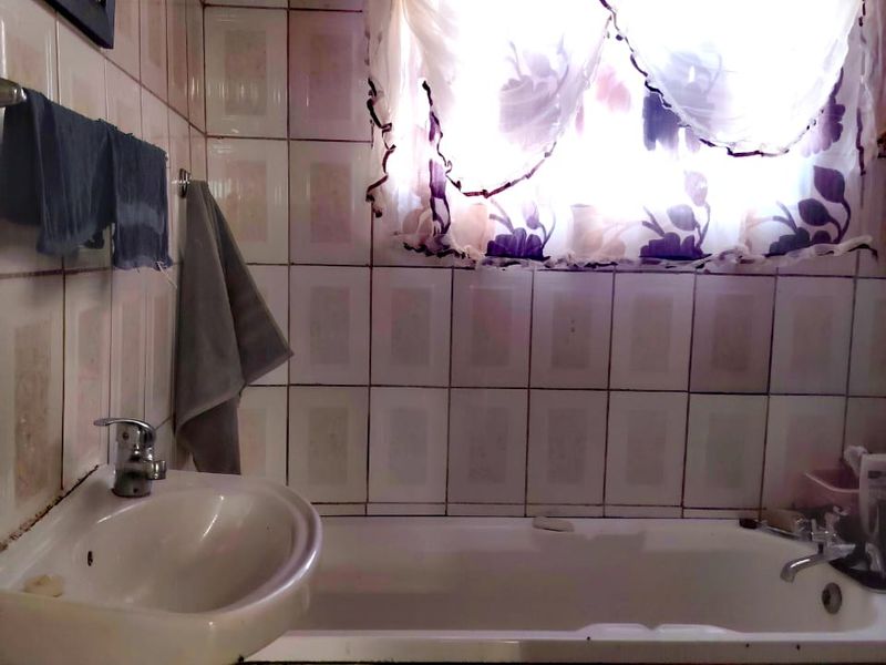 A dated bathroom featuring a wall-mounted basin and a built-in bathtub with full-height ceramic wall tiling.