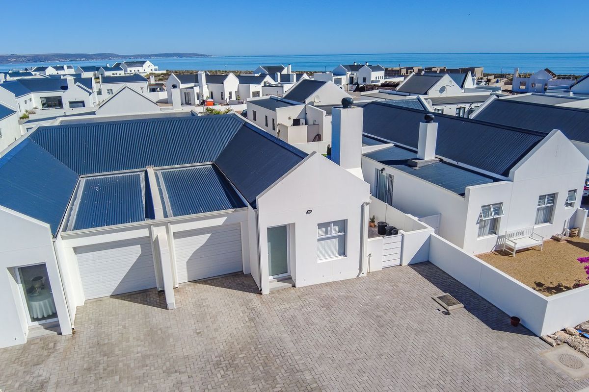 Aerial view of a coastal townhouse complex featuring white facades, dark metal roofing, paved driveways, and double garages with ocean views.