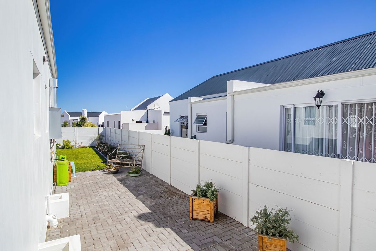 A neat rear exterior area featuring a paved patio, a small lawn, and secure boundary walling, providing a private outdoor space.