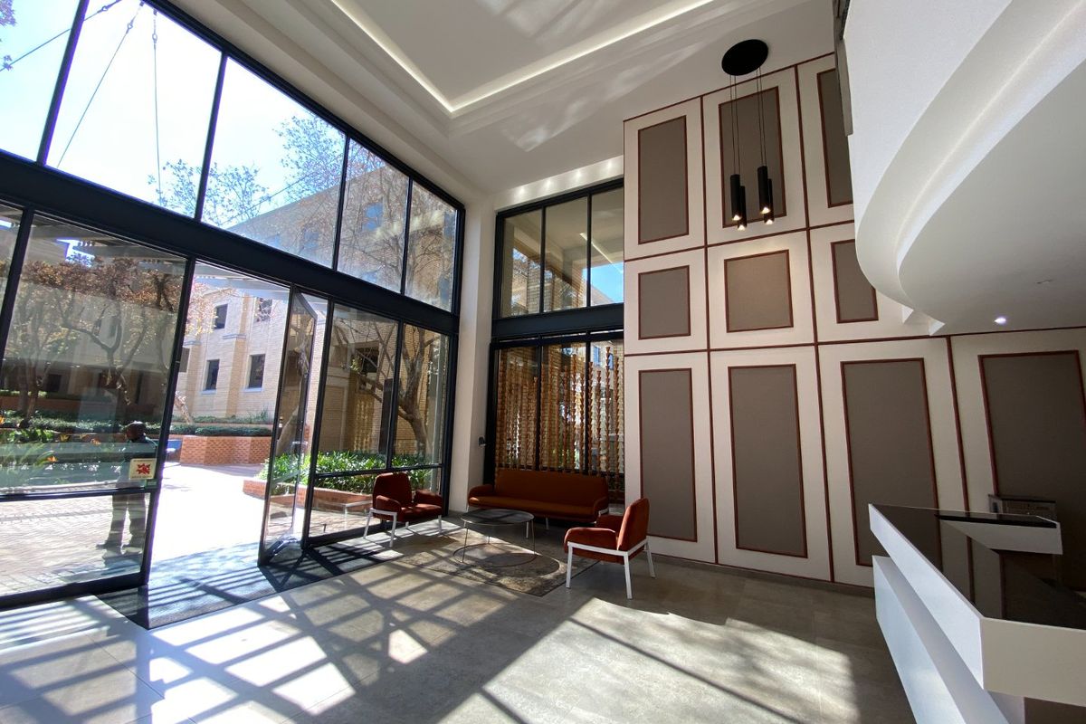 Modern commercial entrance lobby featuring high ceilings, floor-to-ceiling glass windows, decorative wall paneling, and a sleek reception desk.