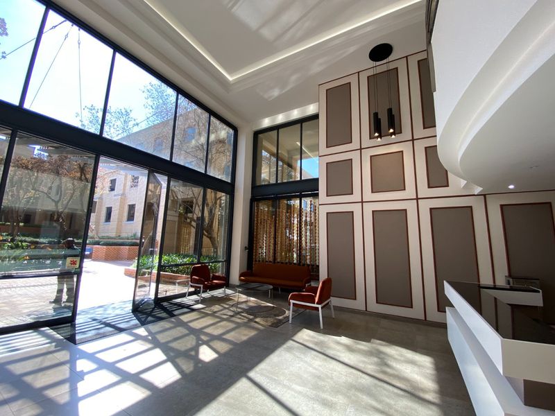 Modern commercial entrance lobby featuring high ceilings, floor-to-ceiling glass windows, decorative wall paneling, and a sleek reception desk.