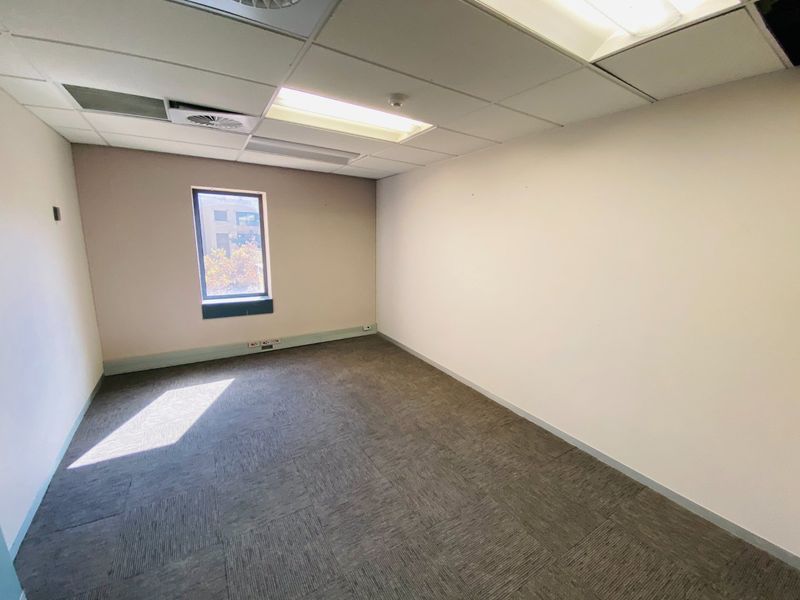 An empty commercial office space featuring carpet tiles, a suspended ceiling with recessed lighting, and an air conditioning vent.