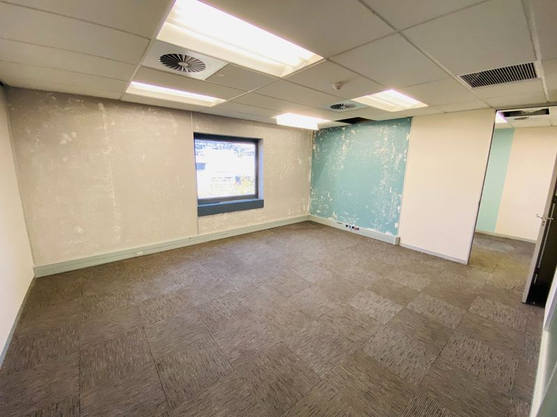 An empty commercial office space featuring carpet tiles, a suspended ceiling with integrated lighting, and air conditioning vents, requiring cosmetic wall repairs.