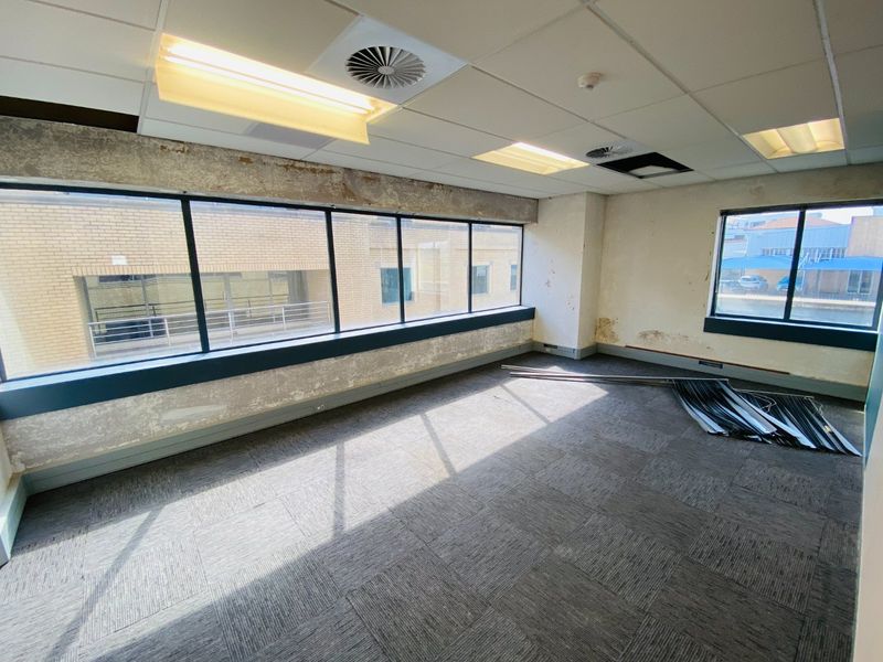 Empty commercial office space featuring large windows, carpet tiles, and a suspended ceiling, currently requiring cosmetic repairs and wall refurbishment.