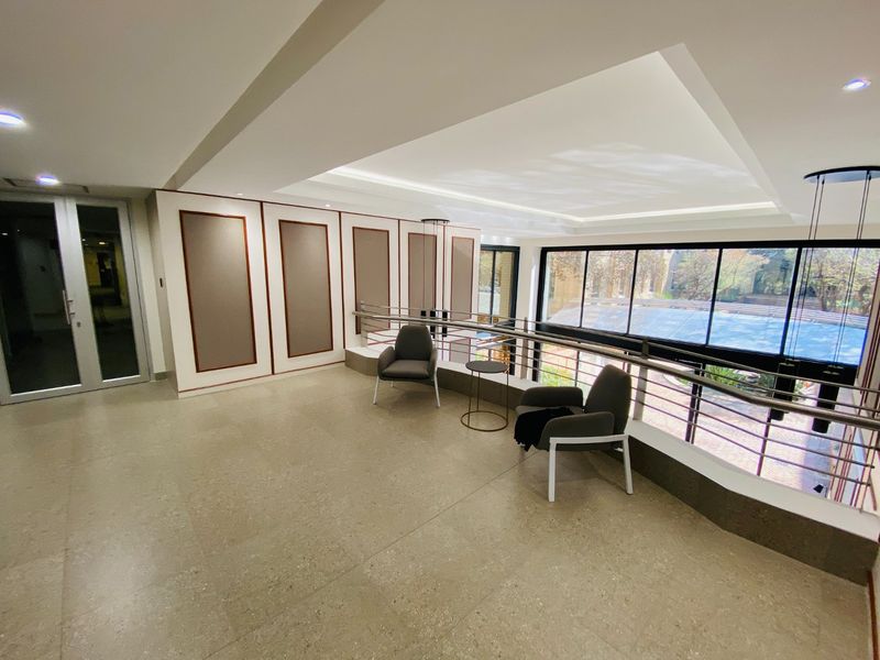 Spacious commercial hallway featuring stone tile flooring, recessed ceiling lighting, and a metal balustrade overlooking the exterior area.